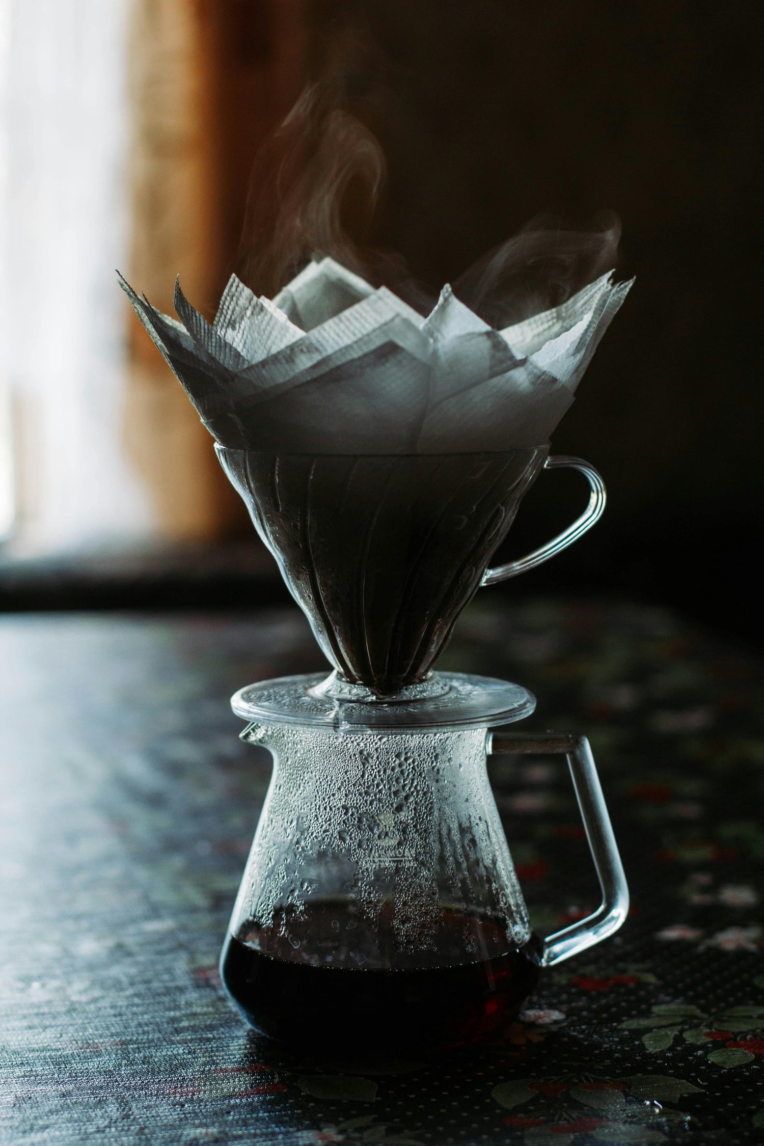 Coffee filter with steam rising from a glass coffee maker on a wooden surface.