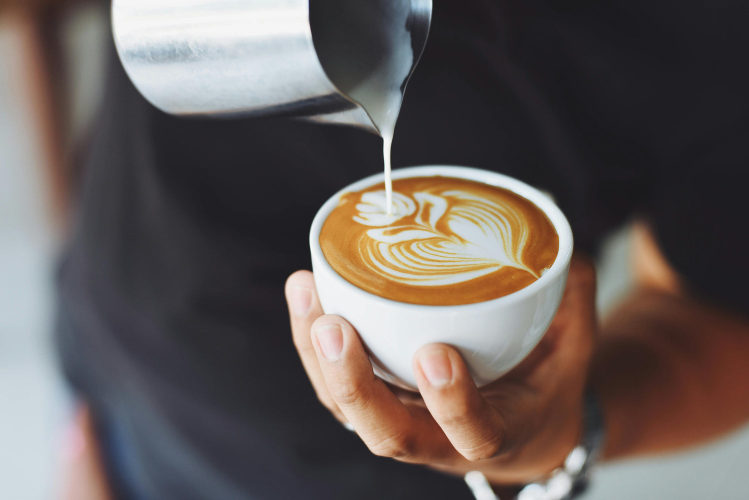 Person pouring milk into a cup of coffee with latte art.