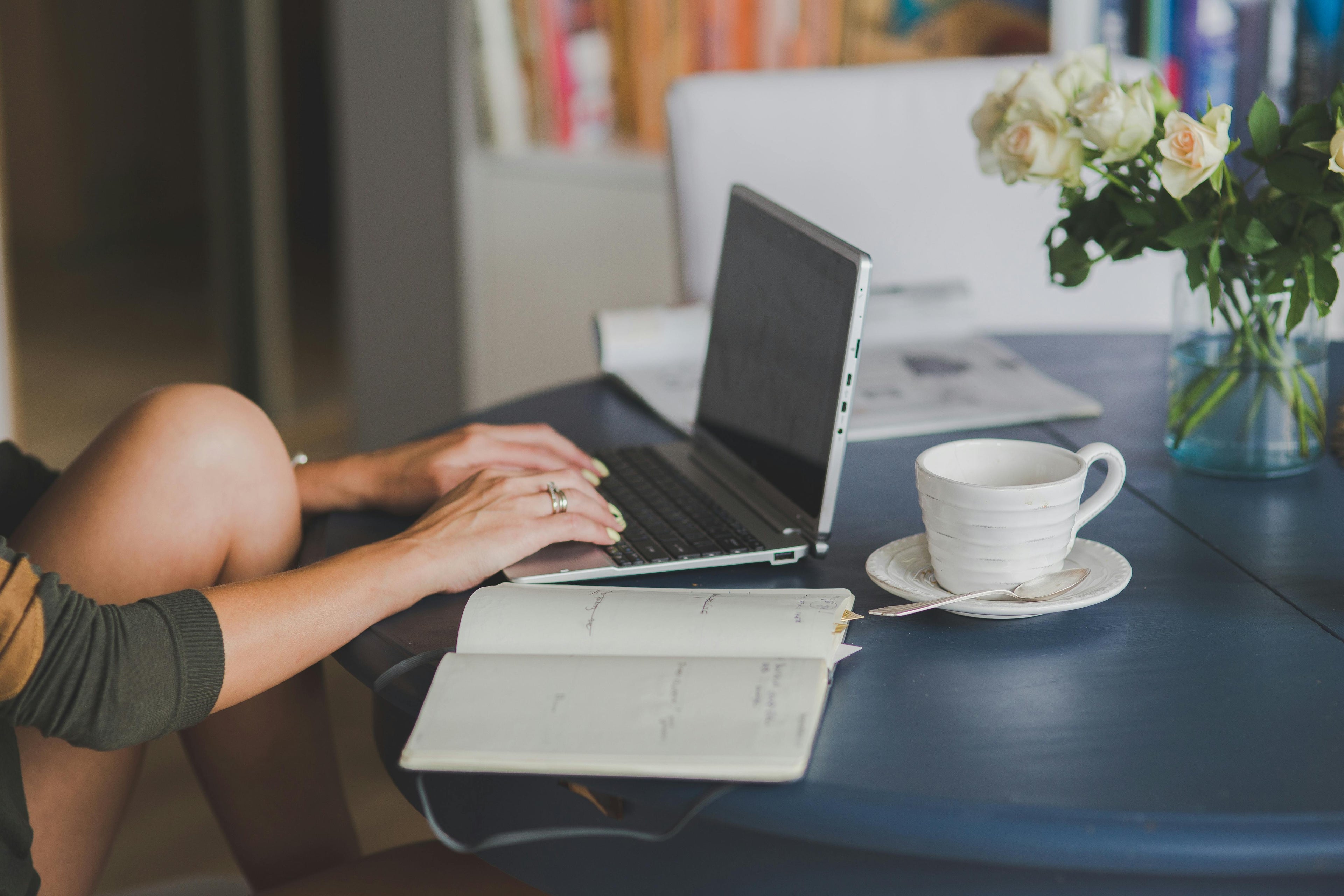 Person using a laptop on a table with a coffee and flowers in the background
