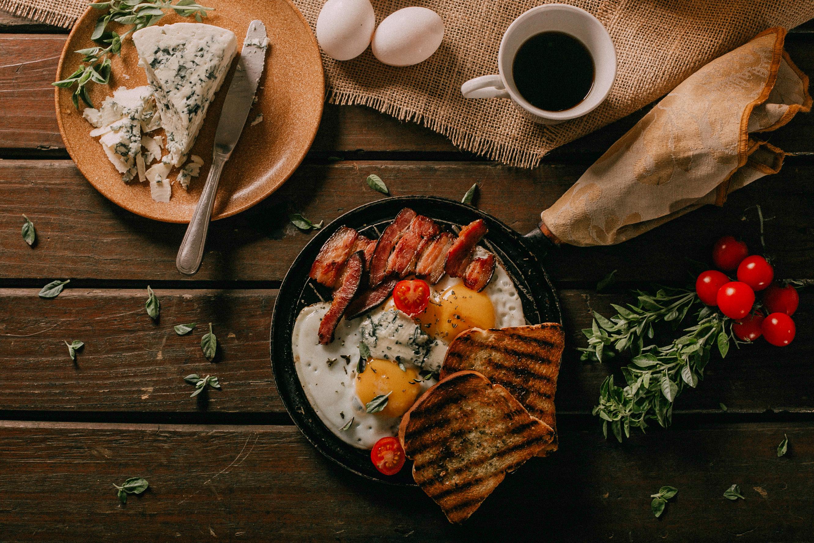 Breakfast setting with eggs, bacon, toast, and a side of coffee on a wooden table.