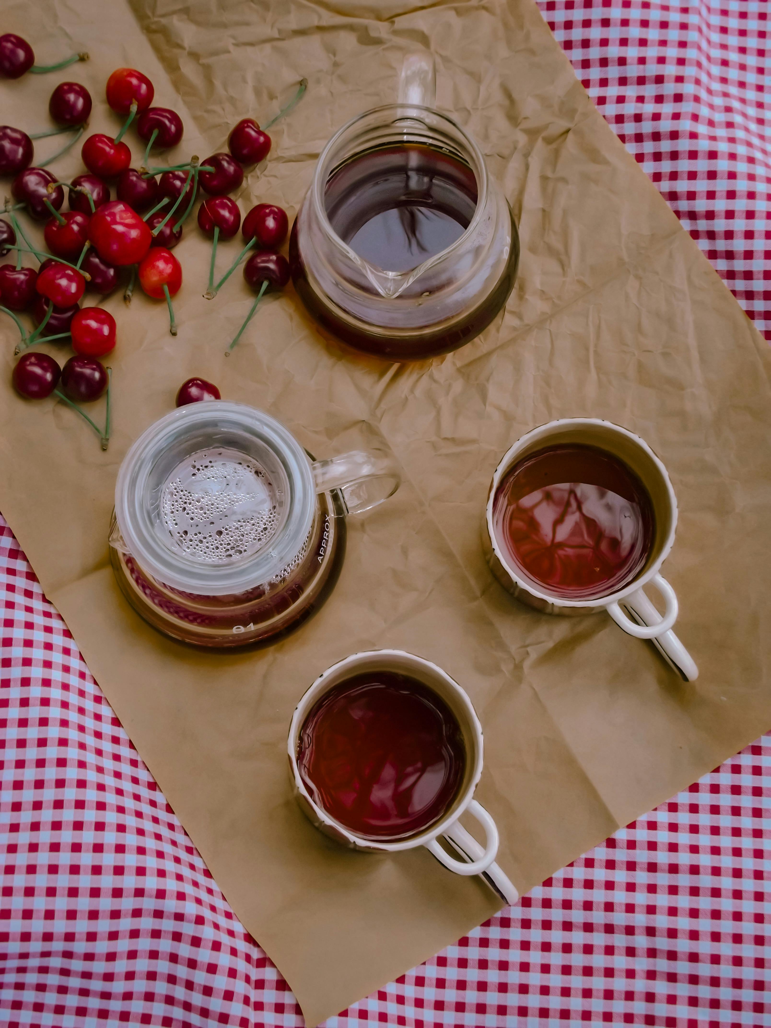 Two cups of tea on a checkered tablecloth with cherries and a jar of honey.
