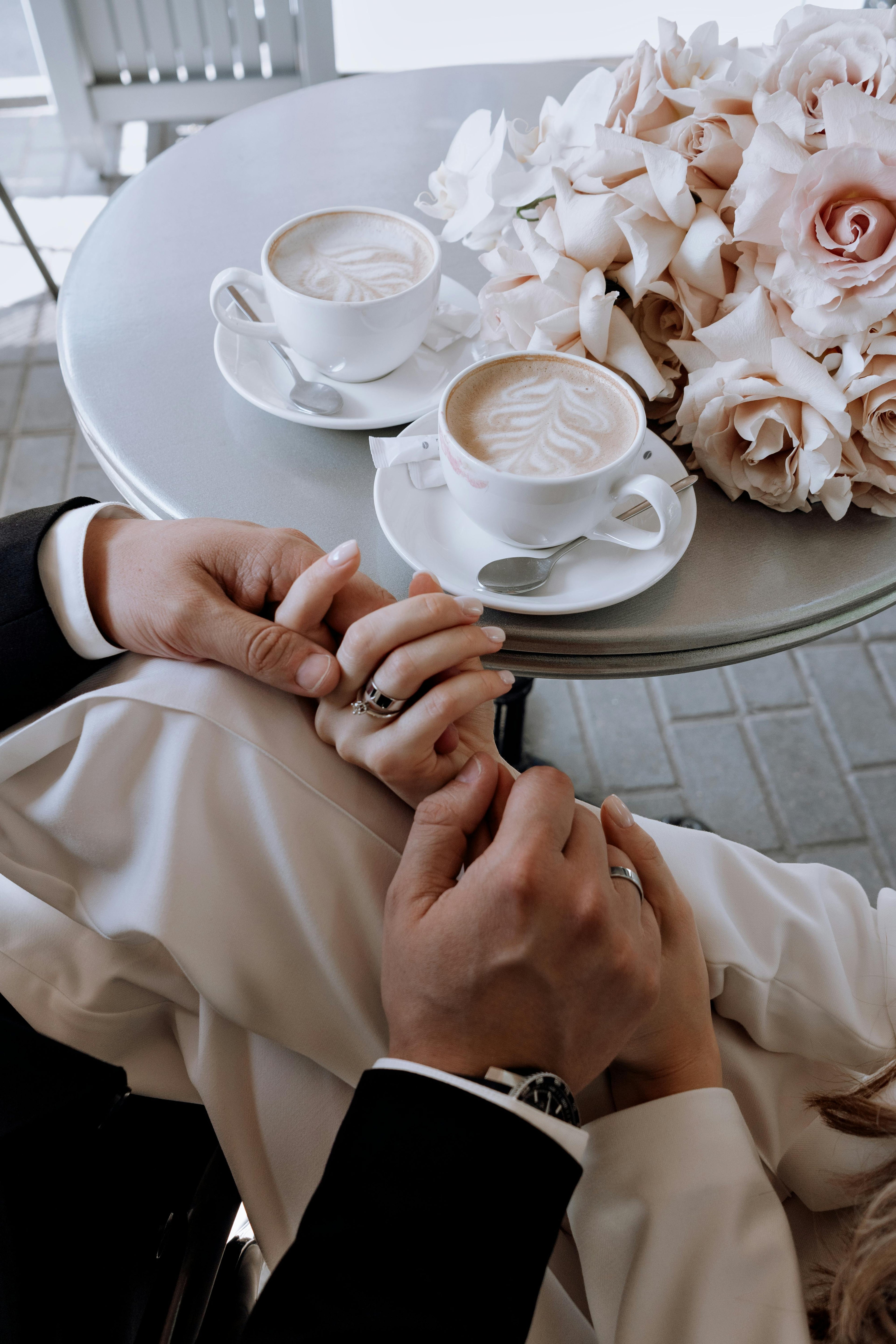 Two people holding hands with a table of coffee and flowers in the background