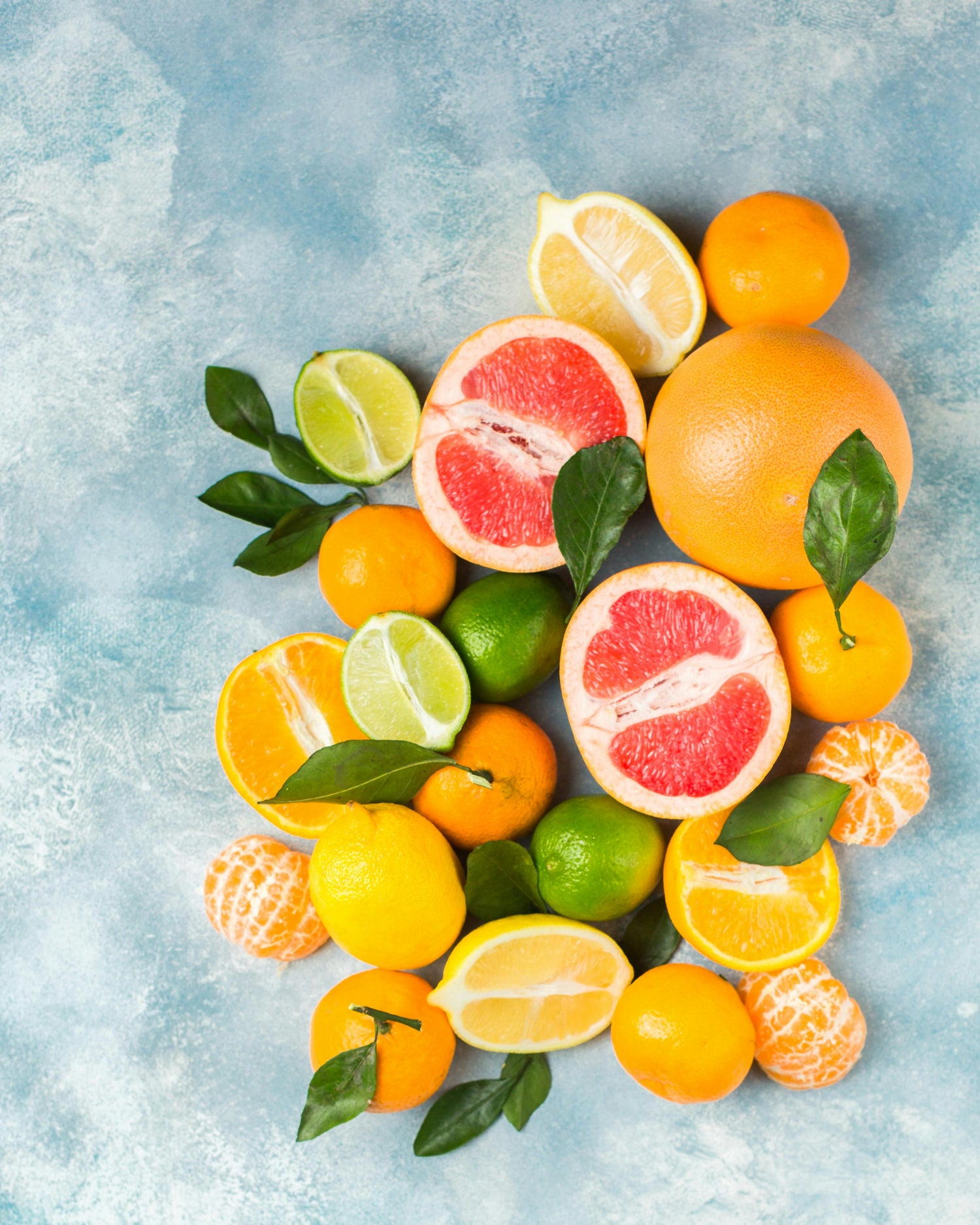 Assorted citrus fruits including oranges, lemons, limes, and grapefruits on a light blue textured background.