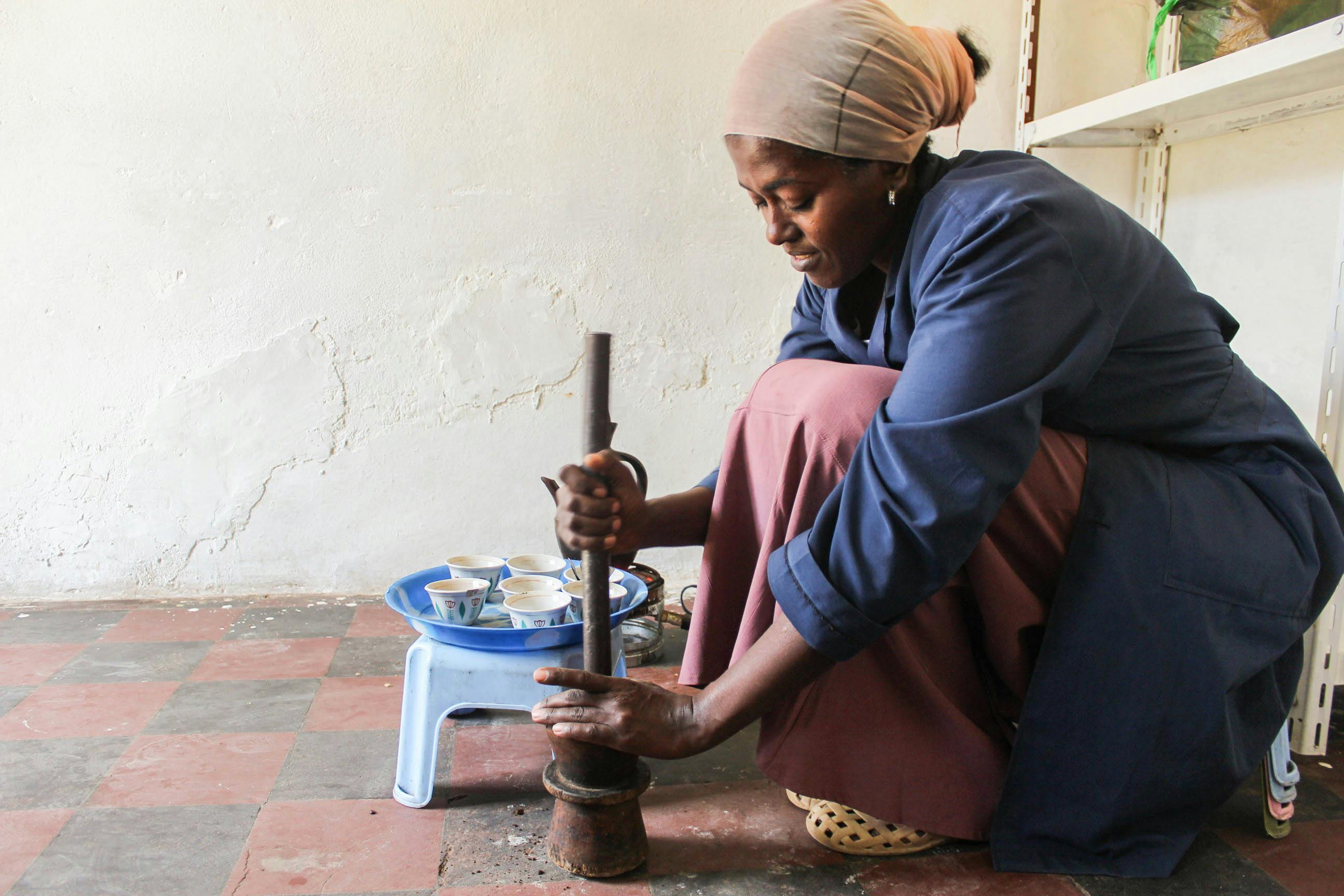 Person using a grinder on a small stool with a white wall background