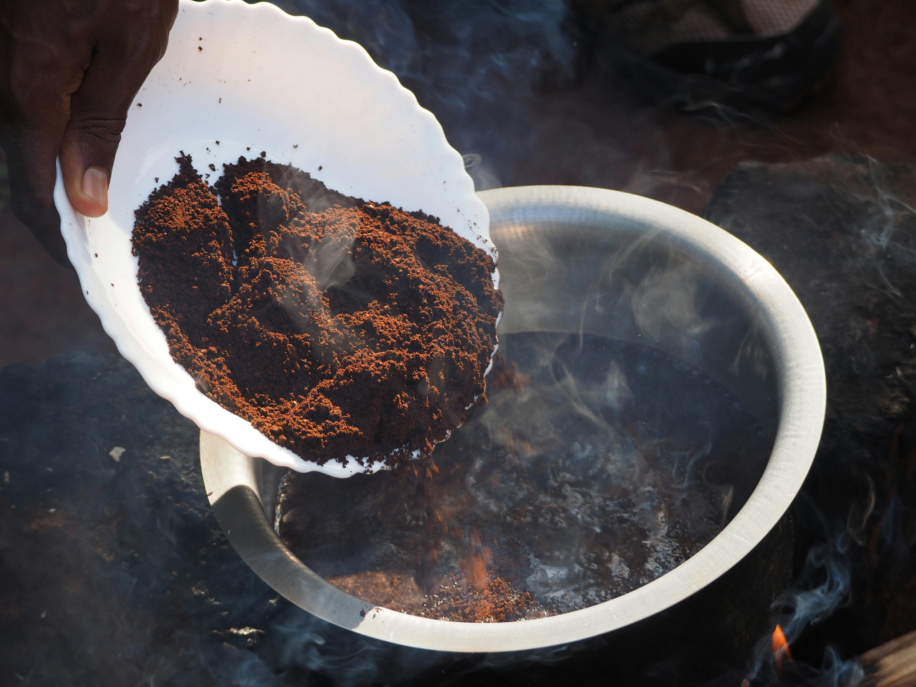 Person holding a white plate with coffee grounds over a pot of boiling water.