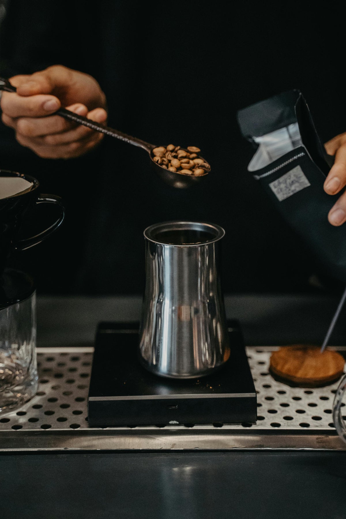 Person pouring coffee beans into a silver container on a dark background