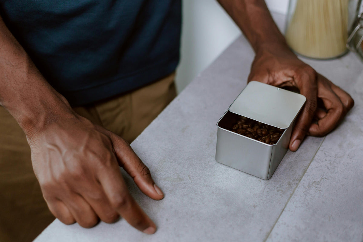 Person pointing at a container of coffee beans on a table
