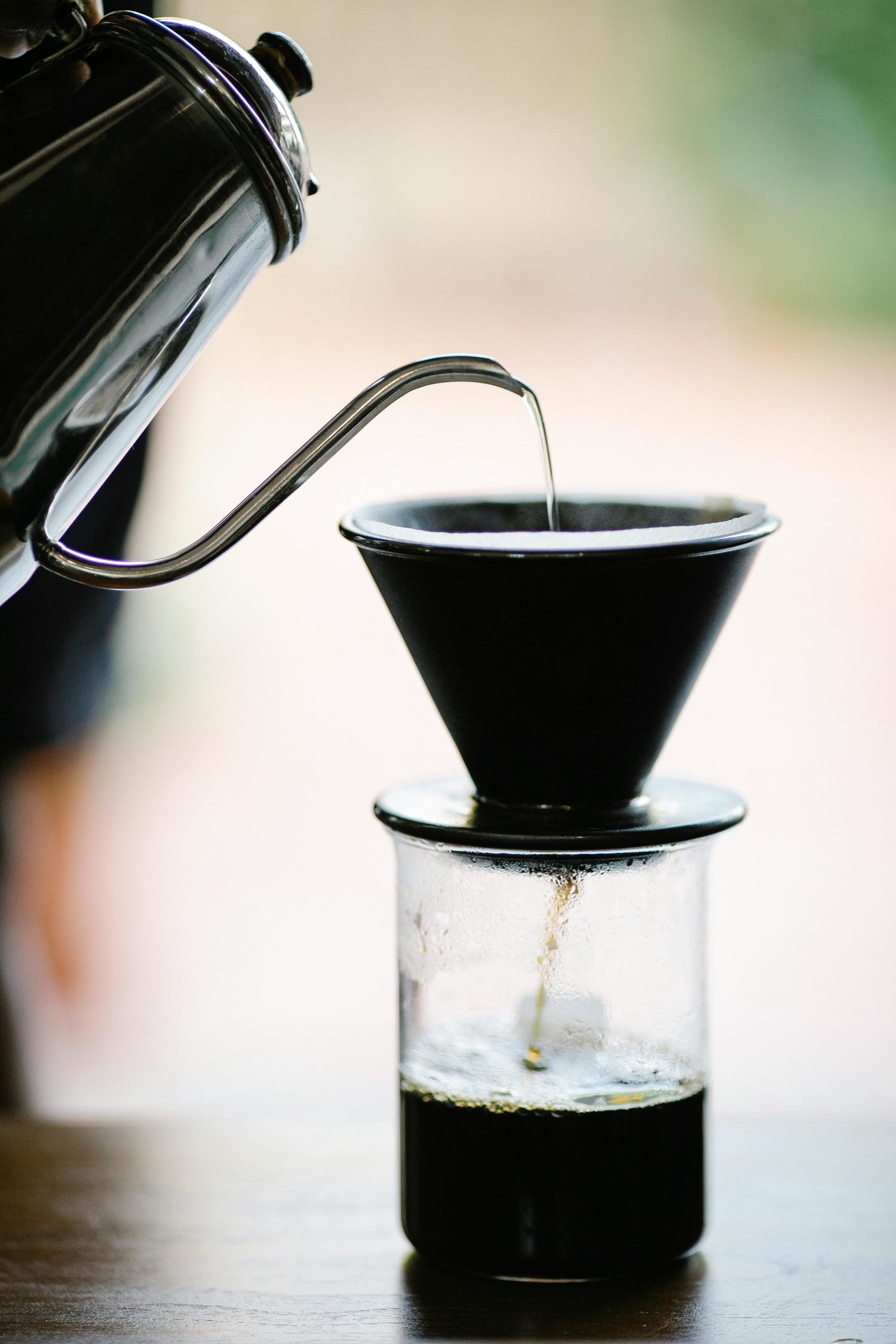 Coffee being poured from a kettle into a black coffee filter over a glass container.