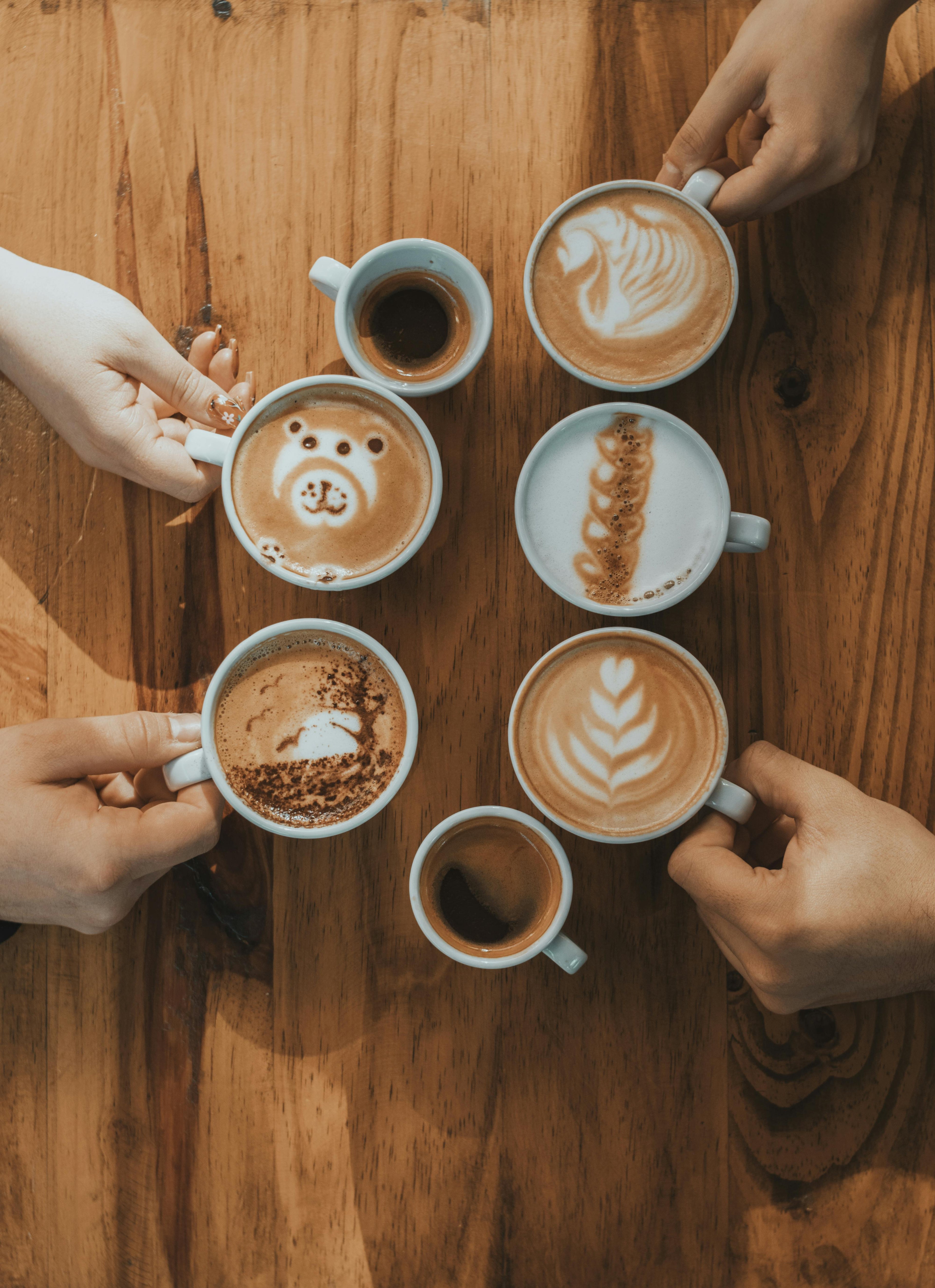 Five coffee cups with different latte art designs on a wooden table.